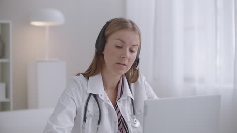 La-Joven-Doctora-Se-Comunica-Con-El-Paciente-En-Línea-Mediante-Una-Computadora-Portátil-Usando-Videollamada-Y-Auriculares-Con-Micrófono